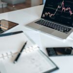 Notebook with digital marketing terms written beside a laptop showing analytics